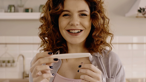 Positive woman holding blurred pregnancy test and  at home