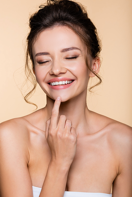 Happy brunette woman touching chin isolated on beige