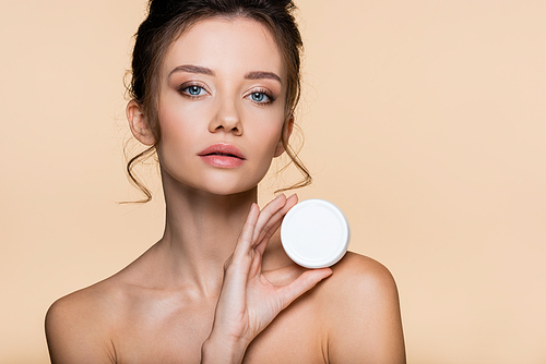 Pretty model with naked shoulders holding container with cosmetic cream isolated on beige