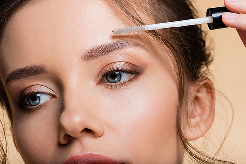 Cropped view of young woman applying eyebrow gel isolated on beige