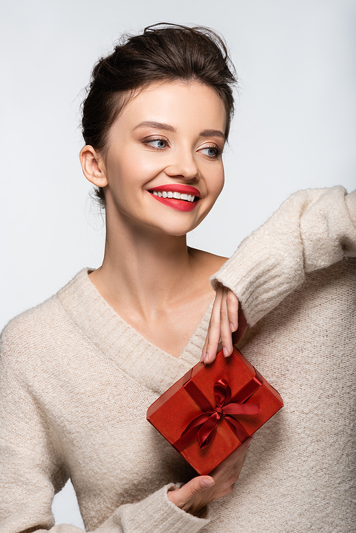 Happy woman in cozy sweater holding red gift box isolated on white