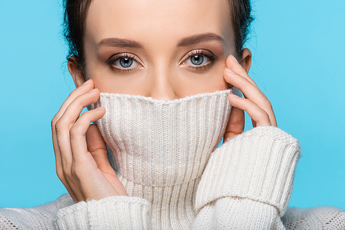 Young woman covering face with warm sweater isolated on blue