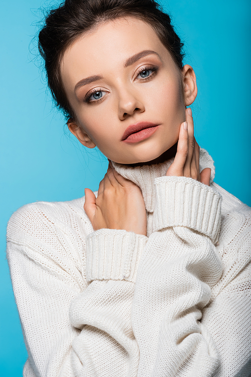 Woman in white warm sweater touching face isolated on blue