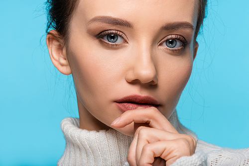 Portrait of pretty woman in sweater holding hand near mouth isolated on blue