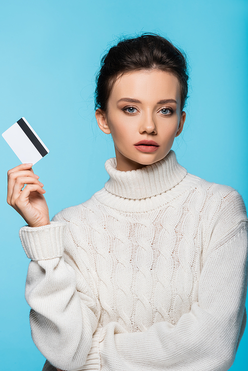 Pretty model in knitted sweater holding credit card isolated on blue