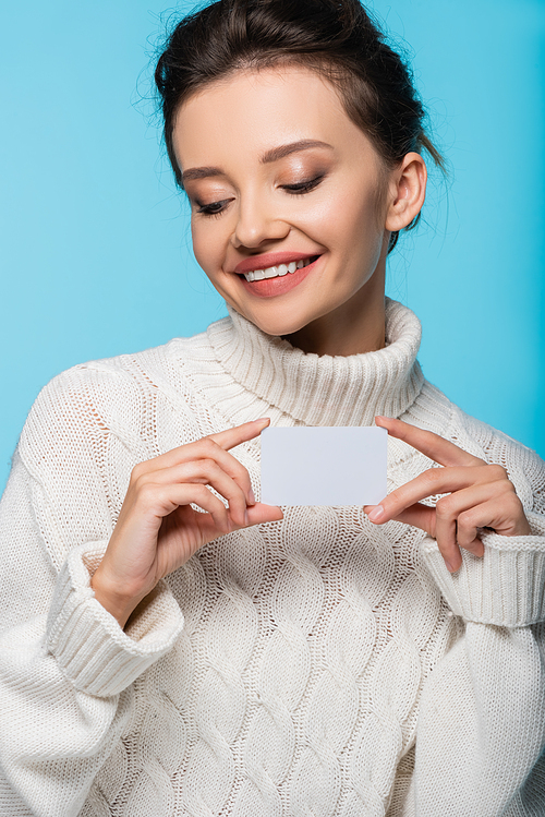 Smiling model in white sweater holding blank card isolated on blue