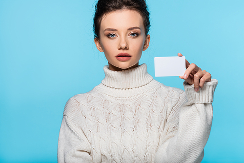 Young woman in knitted sweater holding blank card and  isolated on blue