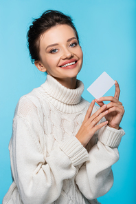 Cheerful woman in white knitted sweater holding blank card isolated on blue