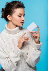 Brunette woman in knitted sweater holding white blank card isolated on blue