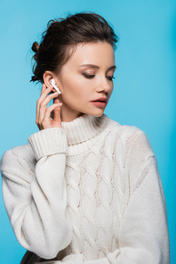 Woman in warm sweater and earphone posing isolated on blue