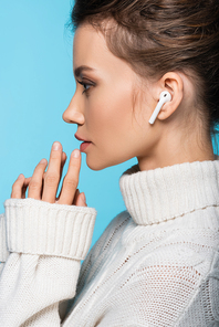 Side view of brunette woman in wireless earphone and sweater isolated on blue