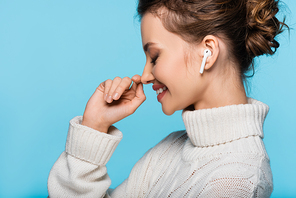 Side view of cheerful woman in knitted sweater and earphone isolated on blue