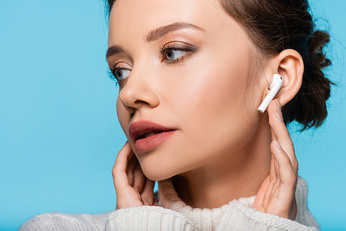 Young model in sweater using wireless earphone isolated on blue