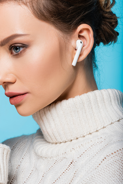 Cropped view of woman in knitted sweater and wireless earphone isolated on blue