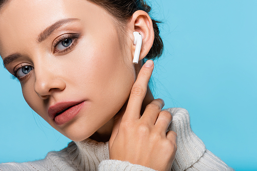 Portrait of young woman pointing at wireless earphone isolated on blue