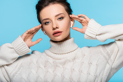 Pretty woman in knitted sweater using earphones isolated on blue