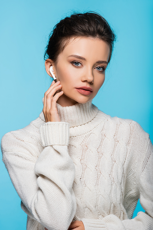 Model in white sweater using earphone and  isolated on blue