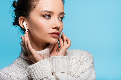 Young woman in knitted sweater and earphone looking away isolated on blue