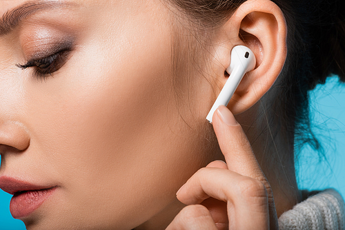 Cropped view of woman using wireless earphone isolated on blue