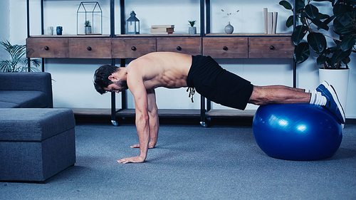 side view of shirtless sportsman training with fitness ball at home