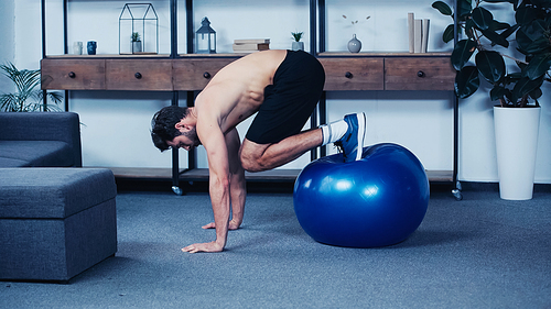 side view of muscular sportsman training with fitness ball at home