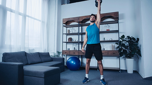 young sportsman in blue tank top exercising with kettlebell at home