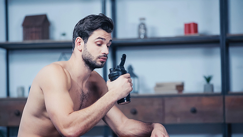 muscular sportsman holding sports bottle at home