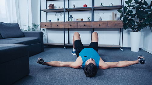 young sportsman lying on floor and exercising with dumbbells
