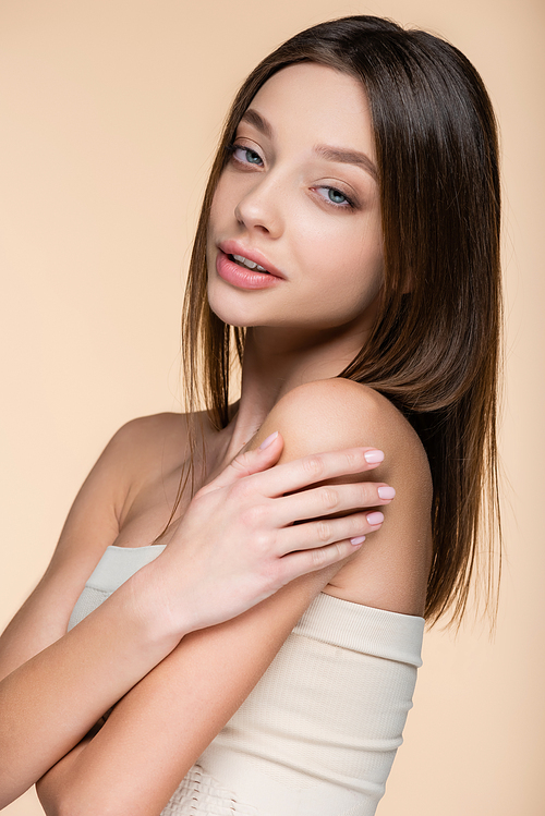 brunette woman in crop top touching bare shoulders isolated on beige