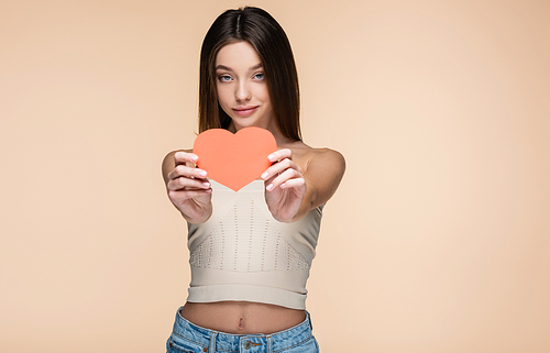 brunette woman in crop top with bare shoulders holding red paper heart isolated on beige