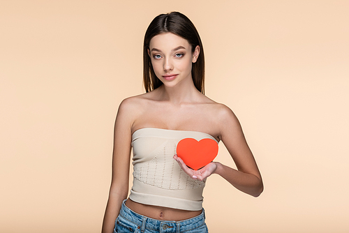 young woman in crop top with bare shoulders holding red carton heart isolated on beige