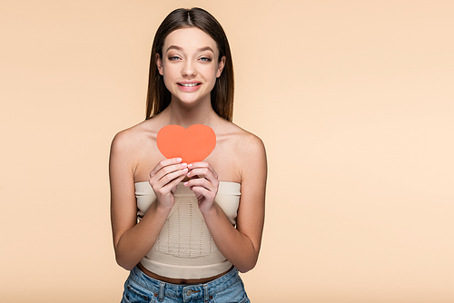 happy young woman in crop top holding red paper heart isolated on beige