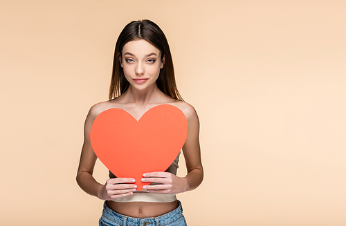 young woman with bare shoulders holding red paper heart isolated on beige