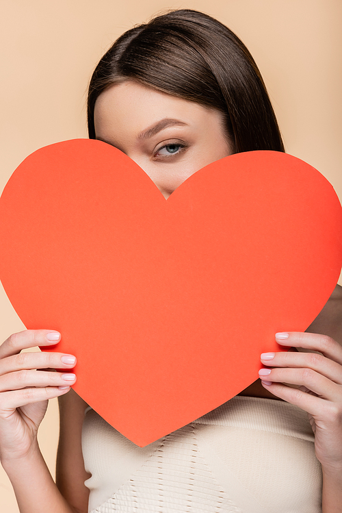 young woman covering face with red paper cut heart isolated on beige