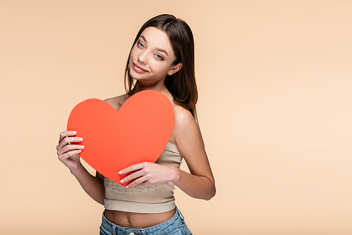 pleased young woman holding red paper heart isolated on beige