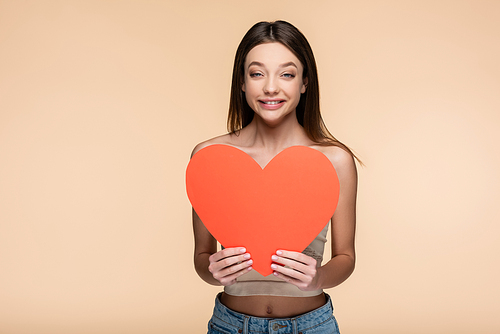 positive young woman in crop top holding red paper heart isolated on beige