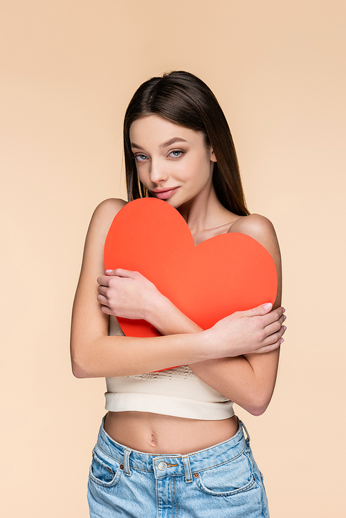 happy woman in crop top hugging red paper heart isolated on beige
