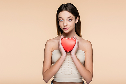 brunette young woman holding red heart-shaped metallic box isolated on beige