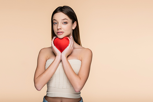 brunette woman holding red heart-shaped metallic box isolated on beige