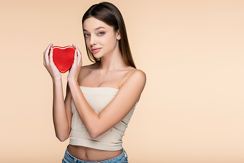 brunette young woman holding heart-shaped metallic box isolated on beige