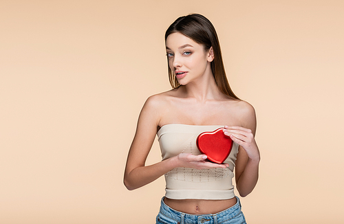 brunette woman holding red heart-shaped box isolated on beige