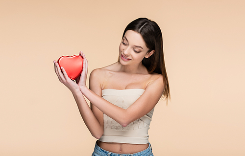 happy young woman looking red heart-shaped metallic box isolated on beige