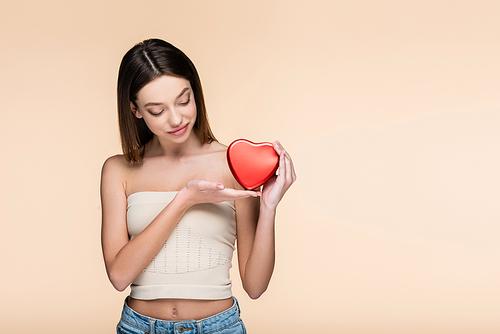 young woman holding red heart-shaped metallic box isolated on beige