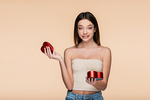 happy young woman holding heart-shaped red box isolated on beige