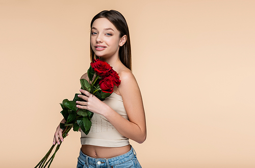 happy young woman in crop top holding red roses isolated on beige