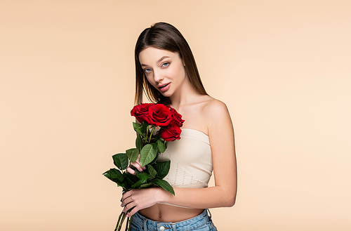 brunette woman in crop top holding red roses isolated on beige