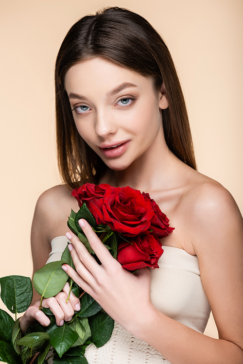 young woman with bare shoulders holding bouquet of red roses isolated on beige