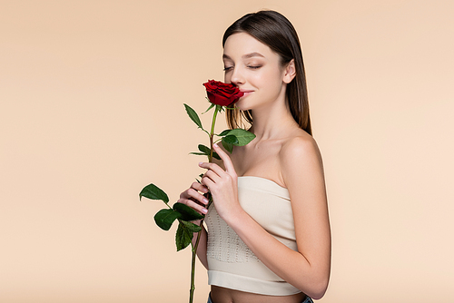 young woman with closed eyes smelling red rose isolated on beige