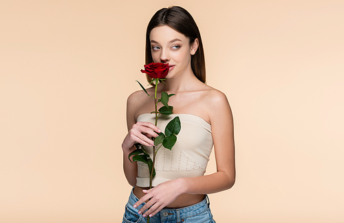 young woman in crop top smelling red rose isolated on beige