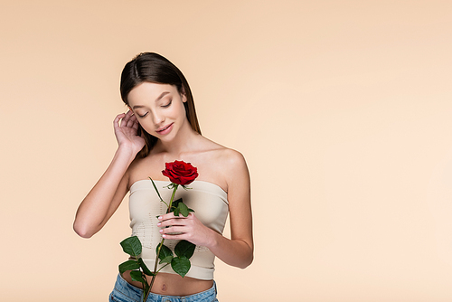 sensual young woman with bare shoulders looking at red rose isolated on beige